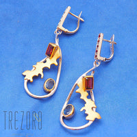 Adventure Road Designer Earrings. Sterling Silver with Garne,t Sapphire. Rhodium and Gold Plated. On blue.